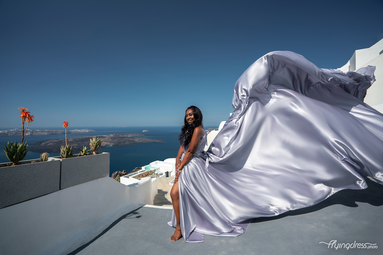 Woman in silver flying dress in Santorini with caldera view and white Cycladic buildings.